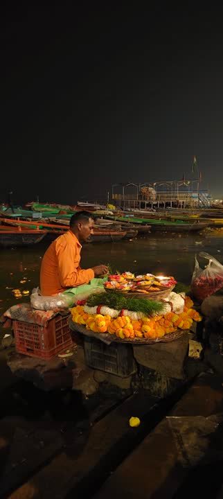 Vendor with marigold offerings on a boat beside the ghat at night