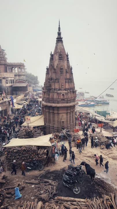 Temple spire above a busy ghat with stacked firewood and boats