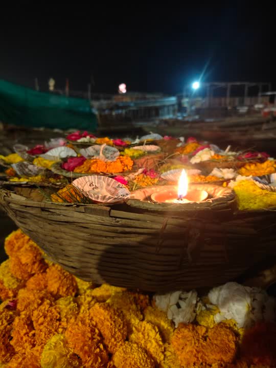 Basket of marigolds with a lit lamp and boats behind at night